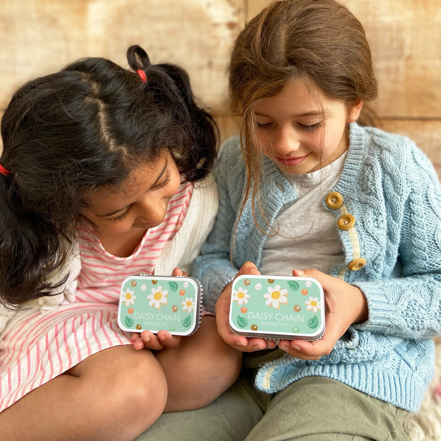 Two young girls proudly displaying their matching tins which is to make a Daisy Chain bracelet by Cotton Twist. Sustainable kids craft.