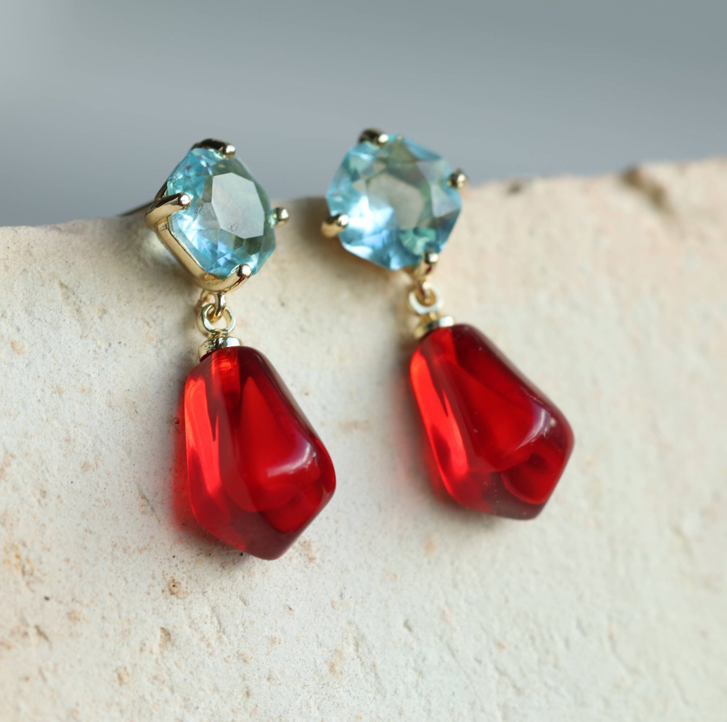 These sweet and colourful earrings feature a light sapphire blue glass jewel in a delicate, with a bright red pomegranate seed charm beneath. These earrings have a stud post fastening with butterfly backs. The blue jewels are made from glass and the pomegranate seeds are made from resin. They measure 30mm (just over one inch) in length and are light and comfortable to wear.