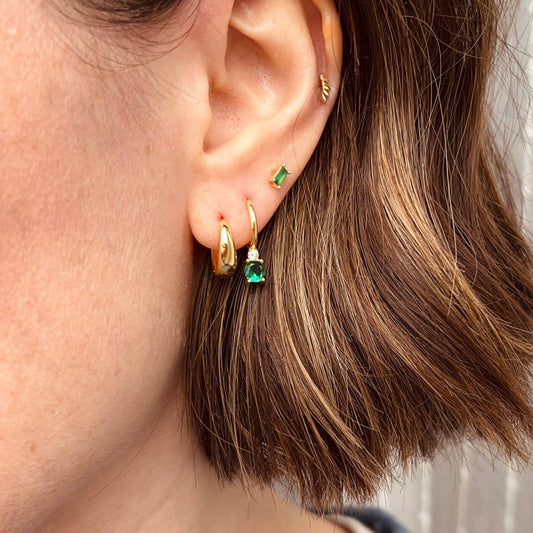 Close-up of Little Nell gold vermeil green diamanté huggie hoops, highlighting the sparkling green stones and delicate design.