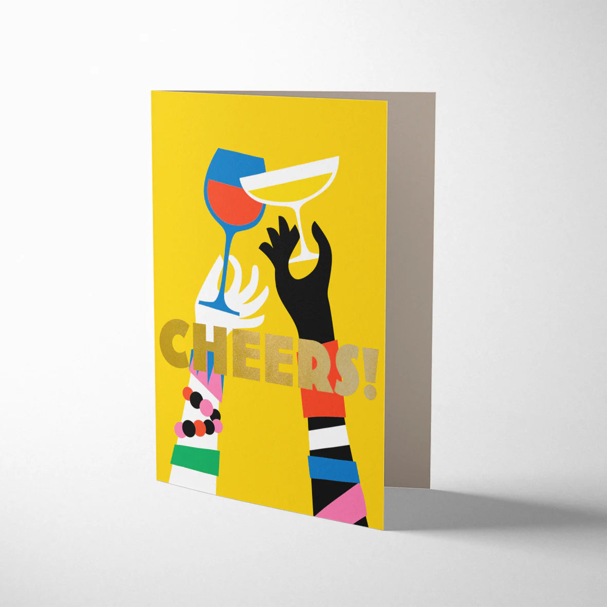 Bright yellow Bureau Alice 'Cheers!' greeting card. Features a graphic illustration of arms with jewellery clinking glasses of fizz and red wine, with 'CHEERS!!' in gold litho lettering.