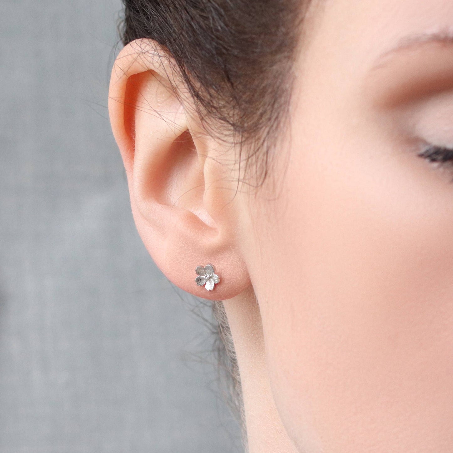 Model wears sweet and dainty stud earrings feature a pair of tiny forget me not flowers, made from Sterling Silver with a subtle brushed texture.