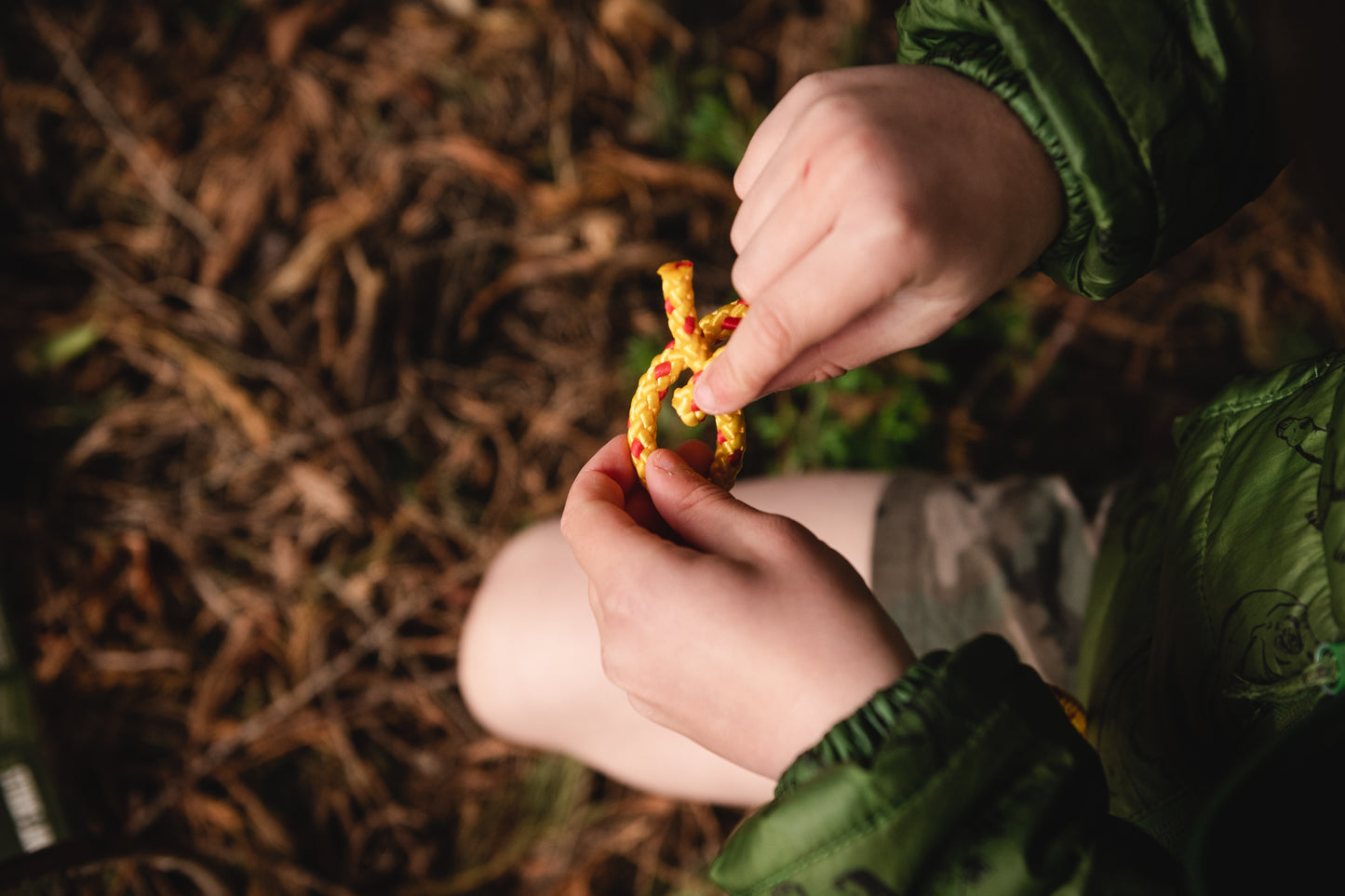 Shows a child's hands learning to tie one of the knots with yellow and red cordage.