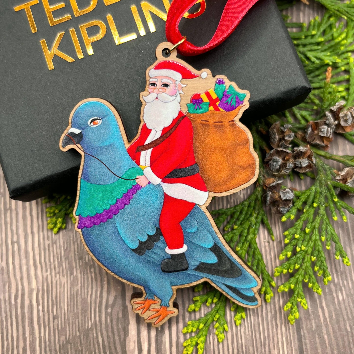 Santa Pigeon wooden Christmas tree decoration with Teddy & Kipling illustration, sustainably certified cherry wood, gold-plated ring, and red velvet ribbon.