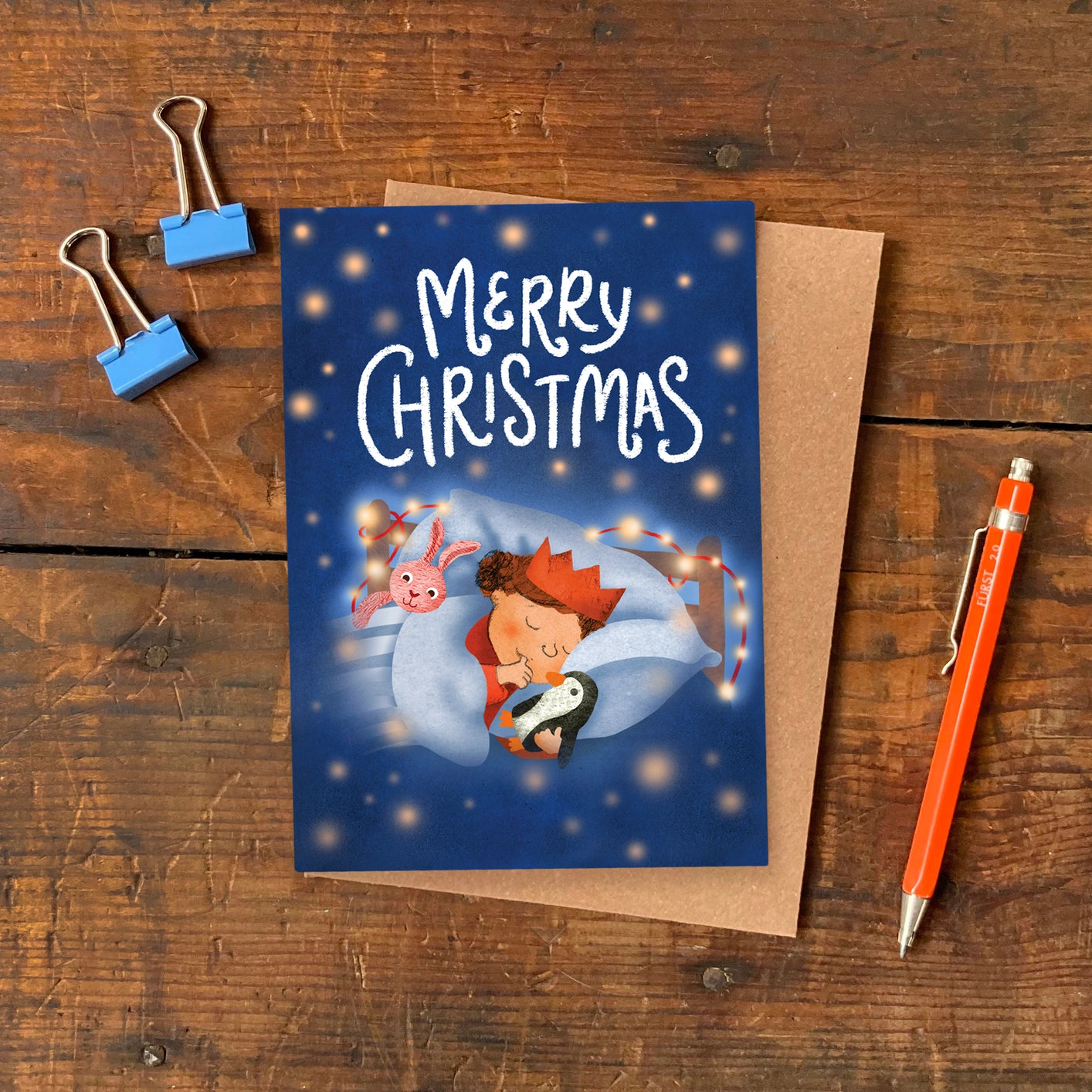 A6 Christmas greeting card with illustration of a sleeping child dreaming of Santa’s arrival, designed by Emily Nash, printed on eco-friendly matte card with kraft envelope.