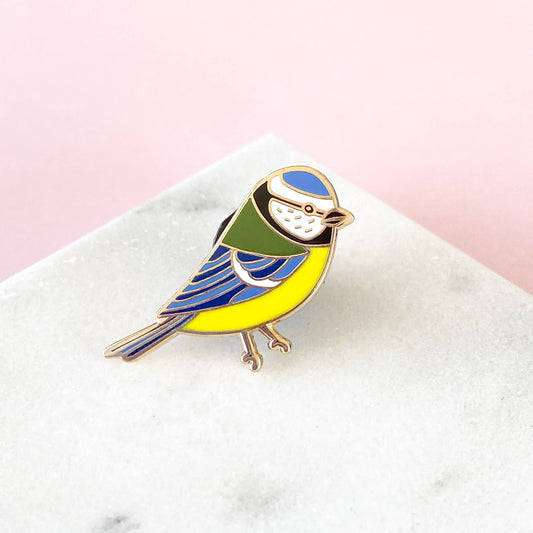 Based on one of Sarah Frances's original illustrations, this Blue Tit Enamel Pin is perfect for any bird lovers! It will add some serious pin flair to any jacket, bag or cardigan.
Made with shiny gold metal and hard enamel, the pin measures 1 inch (25mm) at it's widest point. It has a black rubber clutch on the back and will be presented on a small cardboard backer.