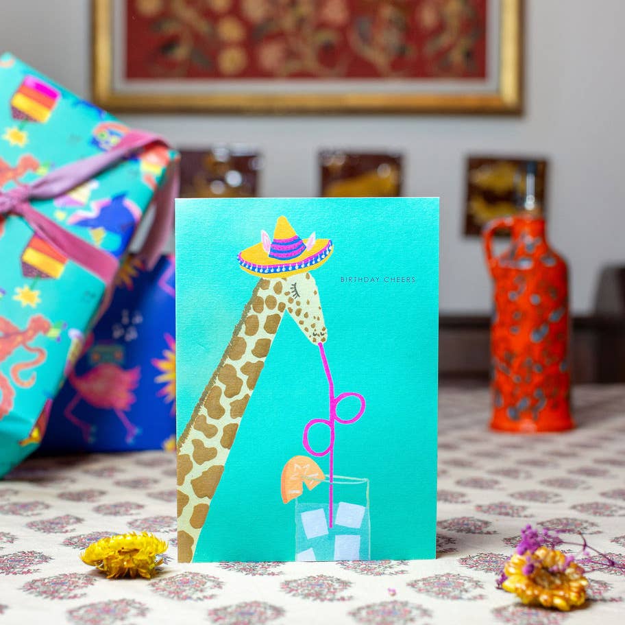 Hand-illustrated ‘Giraffe Cheers’ birthday card showing giraffe in a party hat with ‘BIRTHDAY CHEERS’ text, 5x7”, recycled envelope, UK made.