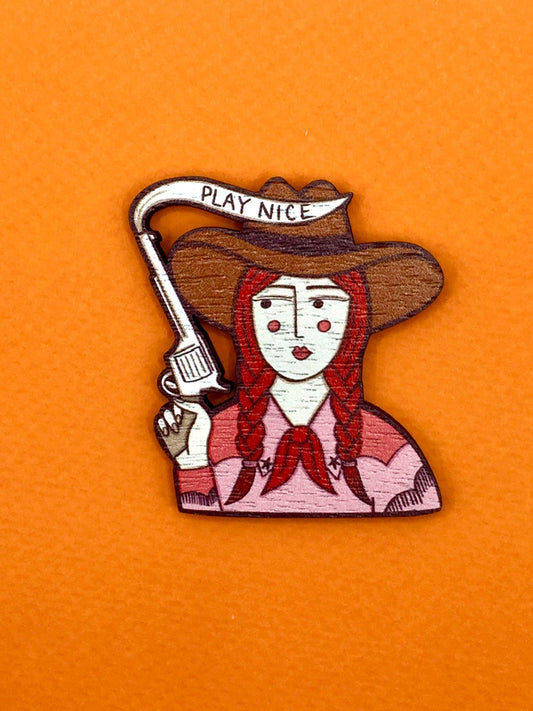 Cowgirl wooden pin brooch with 'Play Nice' message, original illustration by Su Owen, made from sustainable walnut wood, secure metal bar back, UK-made.