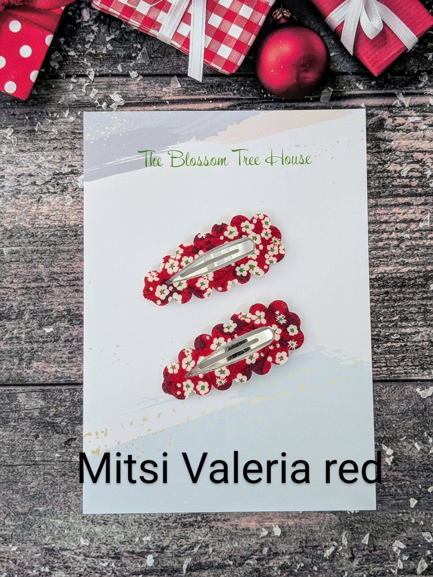 Red hair clips with floral design on a card labeled 'Mitsi Valeria red' against a rustic wooden background.