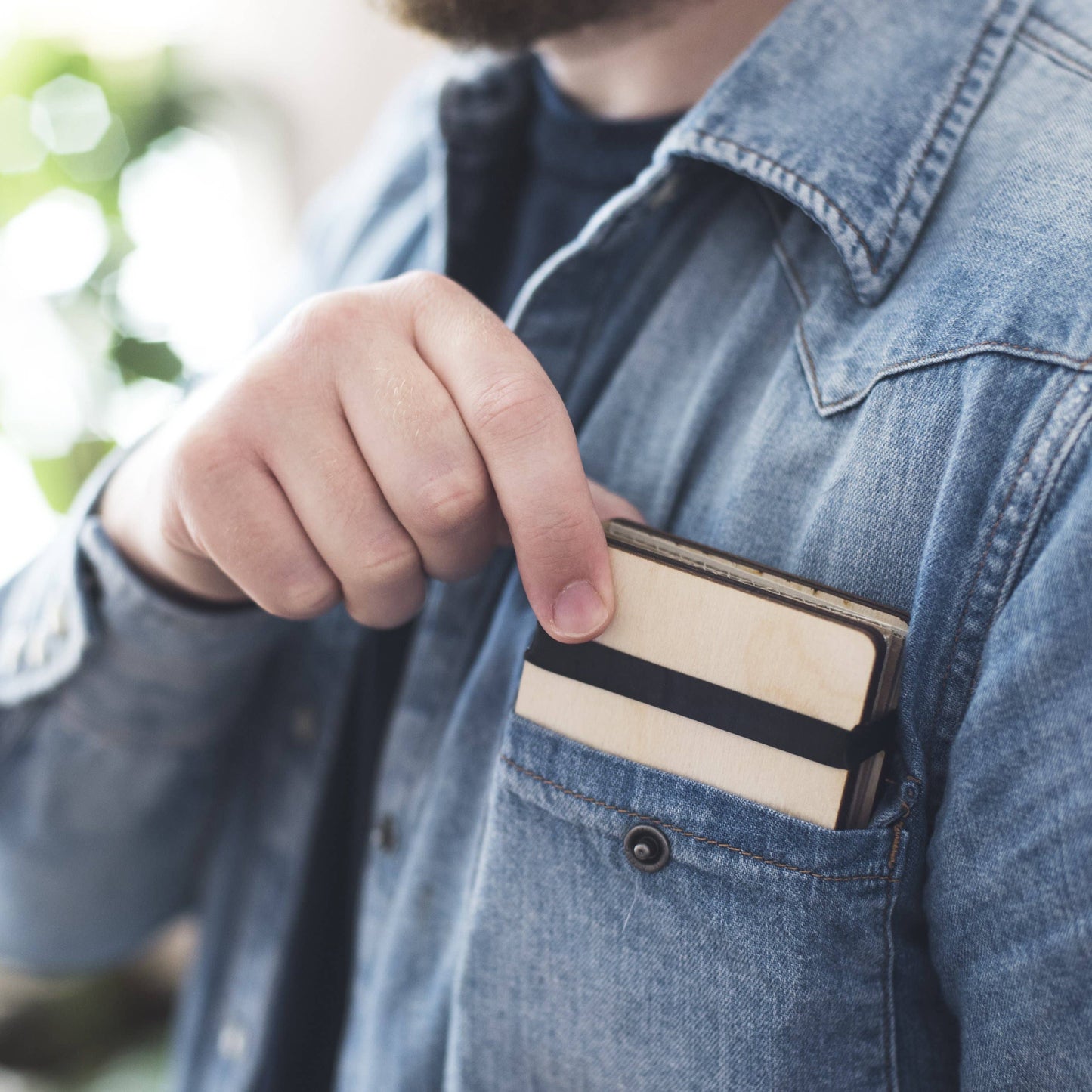 A man wearing a denim shirt, sliding the pocket size flower press by Studio Wald in to his pocket.