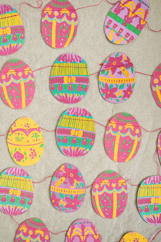 Close-up of vibrant, hand-printed recycled paper Easter eggs on a sewn garland, featuring Spring colours.