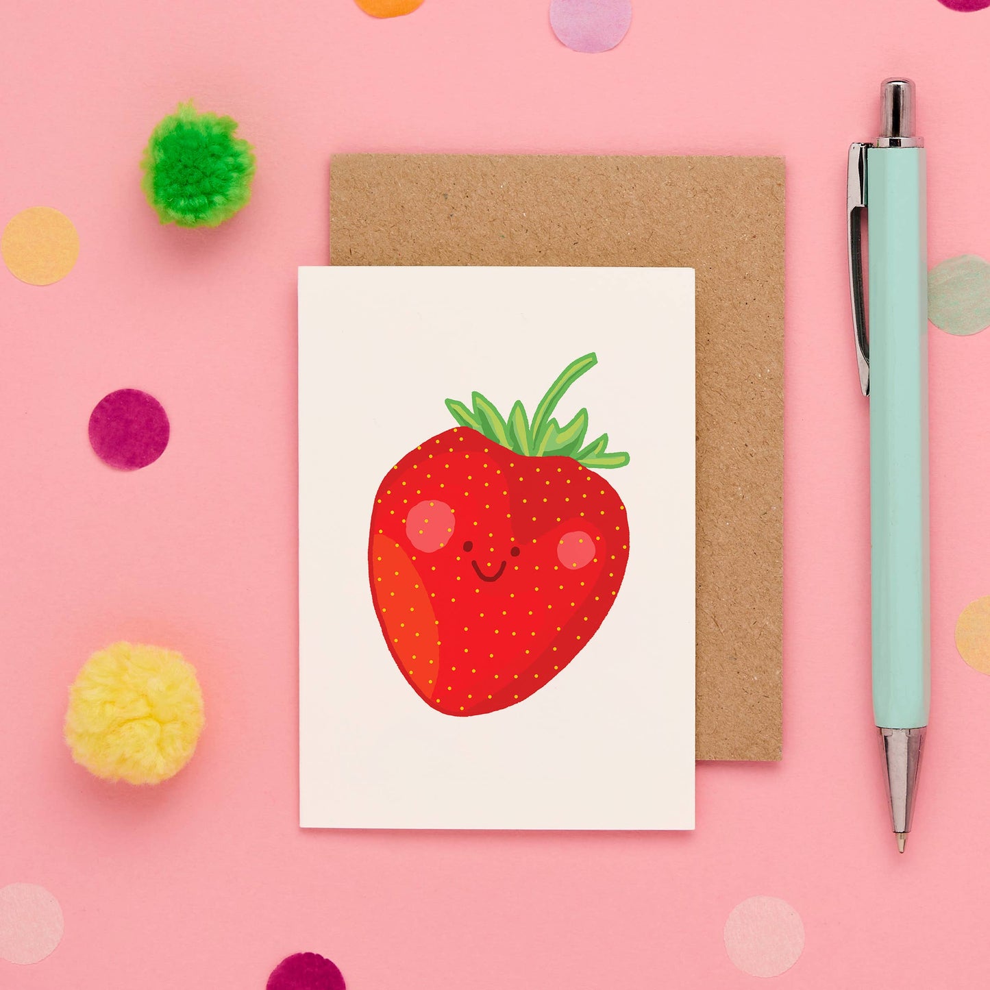 Card with a smiling strawberry design on a pink background with decorative elements and a pen.