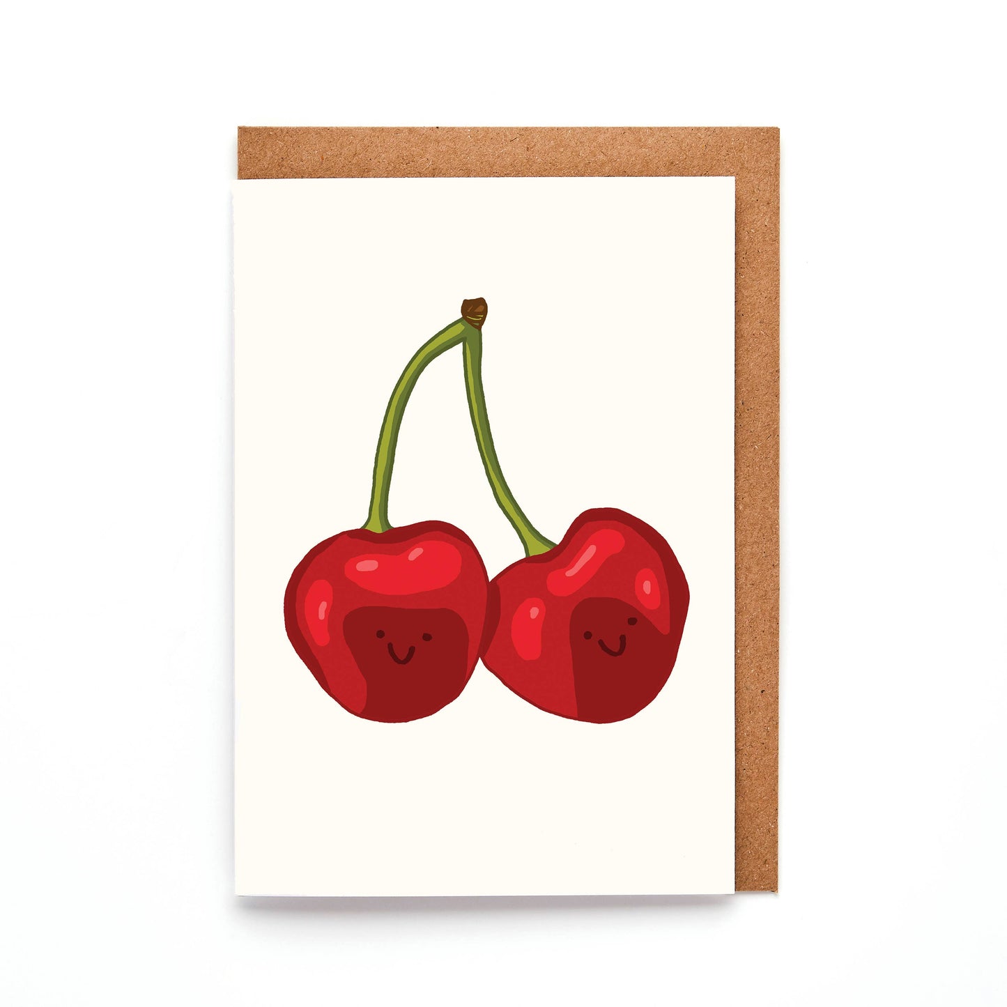 A greeting card with a hand-drawn illustration of two smiling cherries, titled 'Mini Cherries Card'. The card is A7 sized, comes with a brown Kraft envelope, and is blank inside.