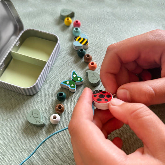 Child's hands threading colourful wooden minibeast beads onto elastic