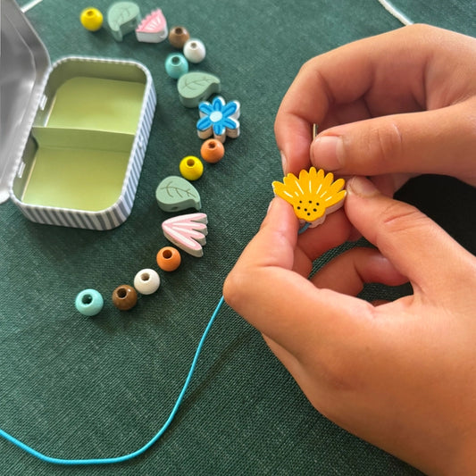 Child's hands creating a wildflower bracelet using the beads and elastic from the craft kit.