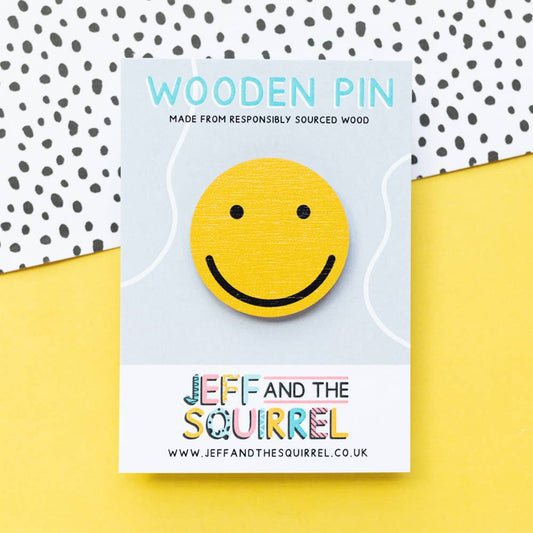 Round wooden pin badge featuring a yellow smiley face, made from sustainable certified birch plywood with a black rubber clutch on a recycled backing card