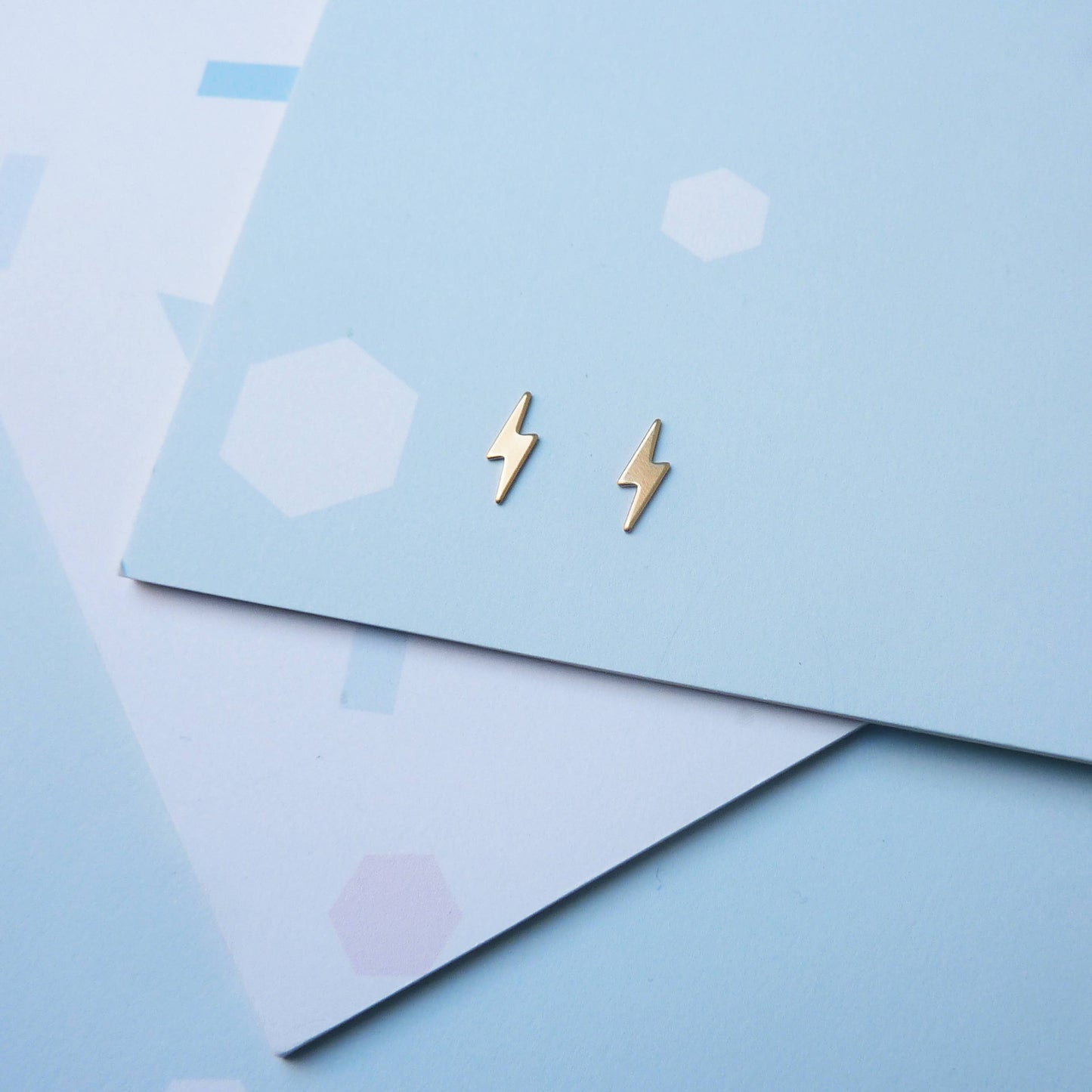 Pair of tiny gold lightning bolt earrings showing scroll backs