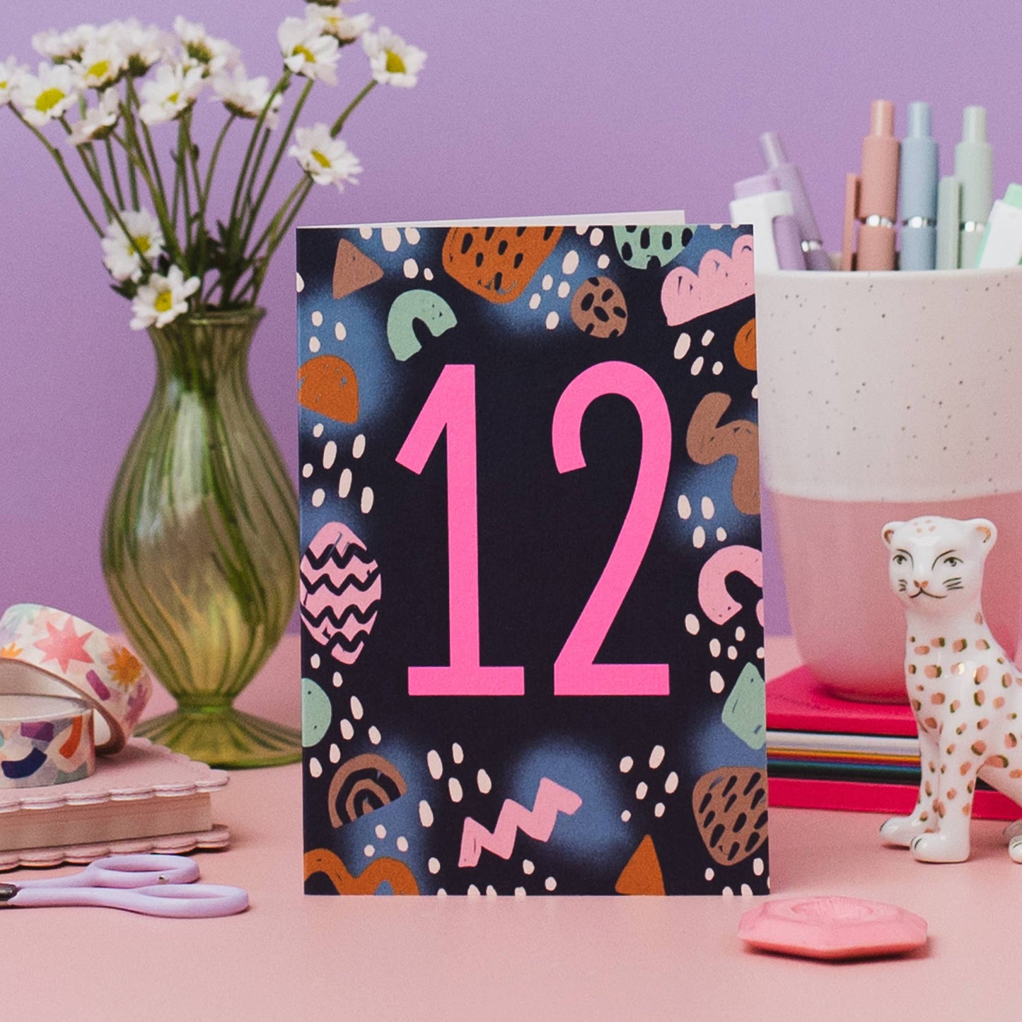 This on trend colour palette and neon pink number makes this milestone birthday card stand out on the shelf. Printed onto premium matt card with a kraft envelope. Illustrated greeting card with abstract shapes pattern and neon pink ink number 12.