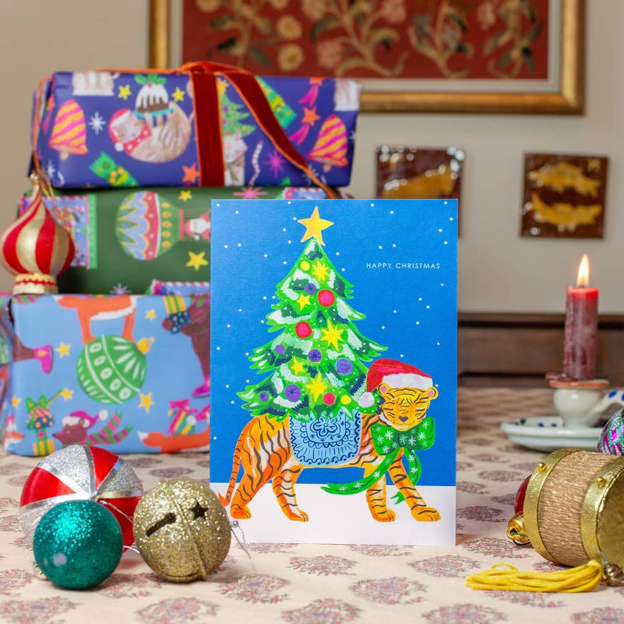 Hand-illustrated 'Tiger in Snow' Christmas card with festive tiger and decorated tree, 5x7”, red envelope, UK made, sustainable.