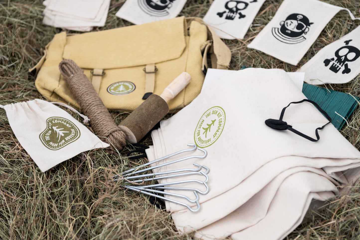 Pirate Den Kit including yellow cotton haversack, cotton calico tarpaulin, waterproof groundsheet, handmade wooden mallet, jute rope, steel tent pegs, pirate eye patch, and Jolly Roger bunting.