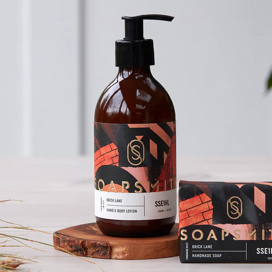 Soapsmith Brick Lane Hand & Body Lotion and matching hand wash, both in amber glass bottles with pumps, on a bathroom shelf. Sustainable beauty.