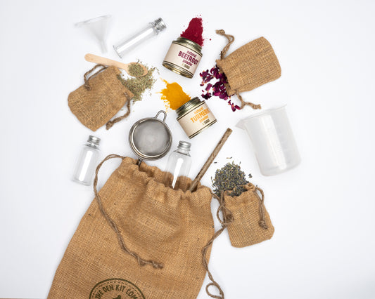 Eco-friendly kids' Potion Making Kit contents laid out, including beaker, sieve, wooden stirrer, funnel, bottles, natural beetroot, turmeric, lavender, rosemary, and rose petals.