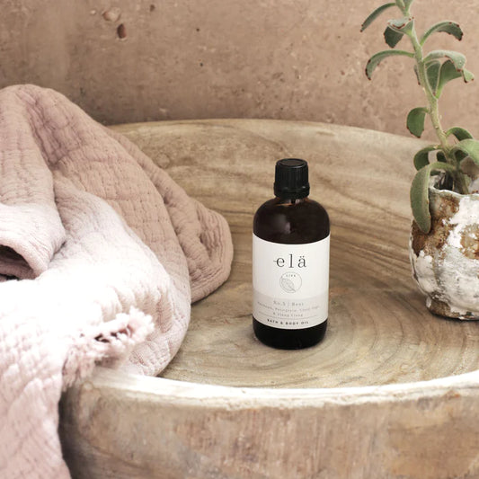 Close-up of Rest No 5 Body & Bath Oil bottle, showing label detail and natural glow