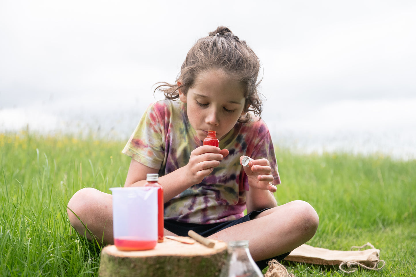 A child smells the bottle of red potion, she has made using the Potion Kit.