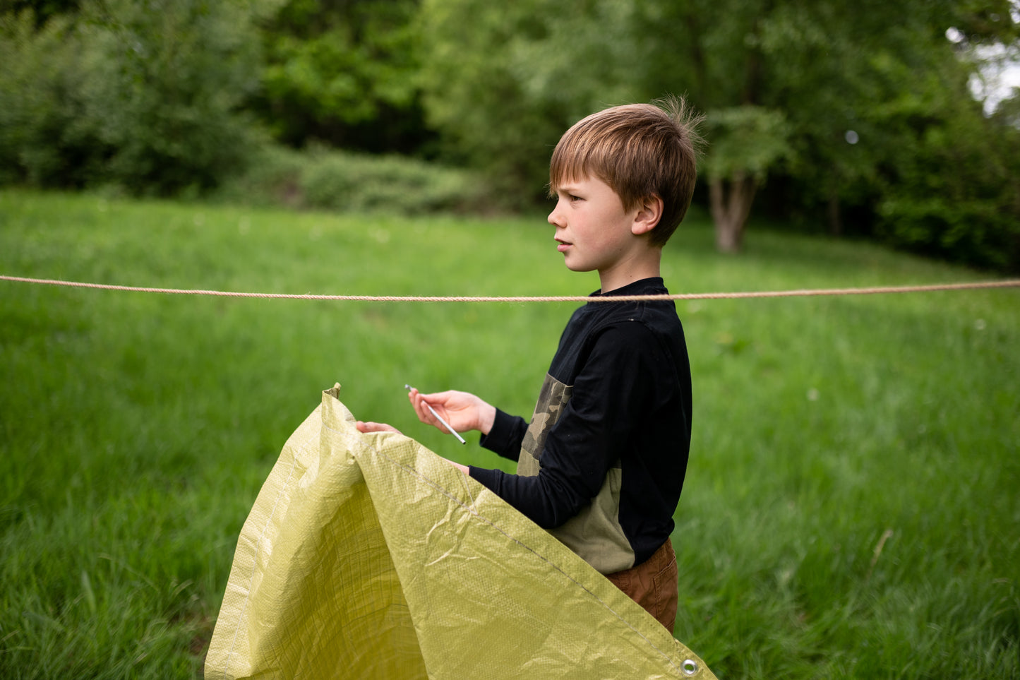 A child actively erecting their den, holding up the camouflage tarpaulin, demonstrating the fun of building with The Original Den Kit.