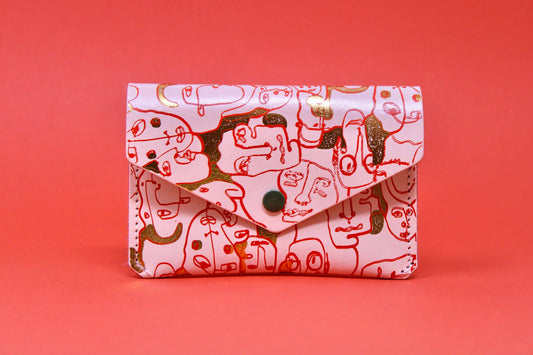 Pale pink leather Many Faces popper purse with gold embossed detail and red accents, featuring unique character illustration.