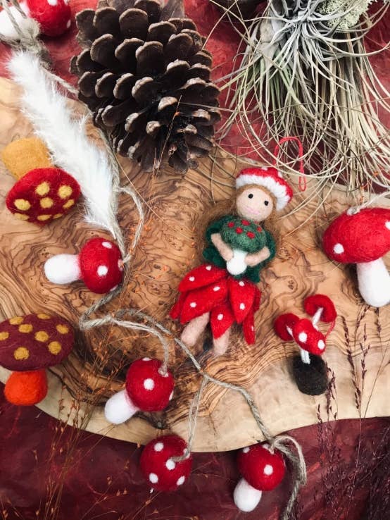 Felted fairy ornament with red mushroom hat and dress on a white background. Handmade felt toadstool fairy autumn hanging decoration with red skirt and hat, sustainable and eco-friendly artisan product.