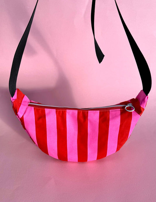 Pink and red striped waxed canvas sling bag, handprinted with artisan detail, featuring adjustable buckle straps and water-resistant finish.
