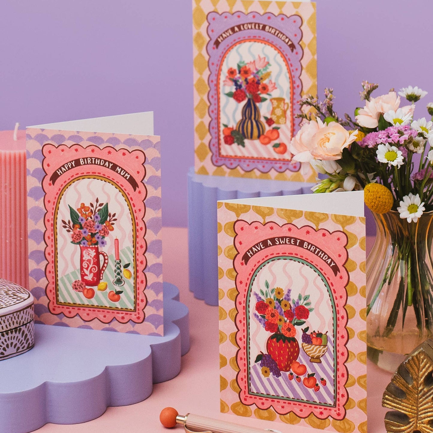 Hand drawn lettering reads 'Have a sweet birthday'. Part of the on trend Harlequin range, which features contemporary vases of flowers and fruit in a patterned tablescape. A6 size illustrated greeting card with tile pattern and vase of flowers and fruit illustration, printed onto premium textured card with a kraft envelope.