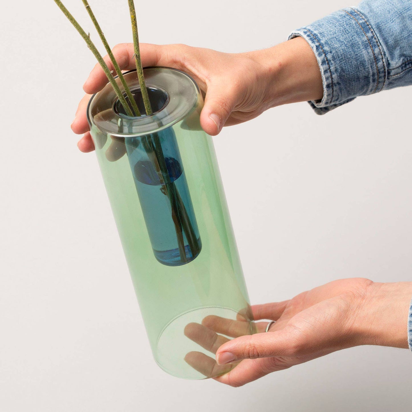 Person holding a cylindrical green vase with a reflective surface against a plain background