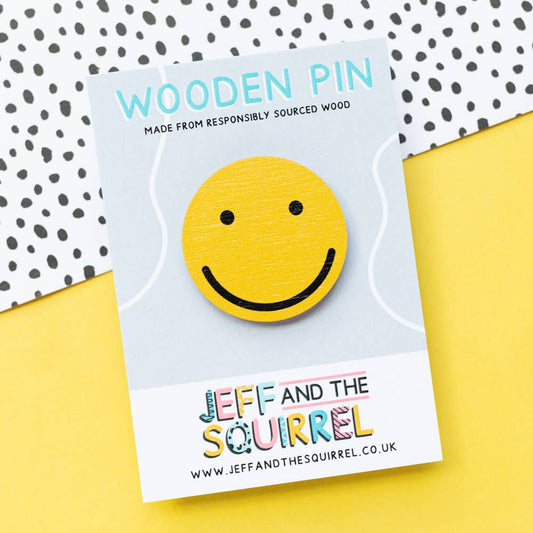 Yellow smiley face wooden pin badge, 40mm, made from sustainably certified birch plywood with a black rubber clutch, displayed on recycled backing card