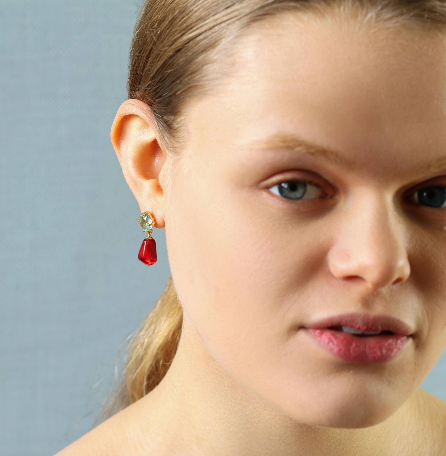 Model wears these sweet and colourful earrings feature a light sapphire blue glass jewel in a delicate, with a bright red pomegranate seed charm beneath. These earrings have a stud post fastening with butterfly backs. The blue jewels are made from glass and the pomegranate seeds are made from resin. They measure 30mm (just over one inch) in length and are light and comfortable to wear.
