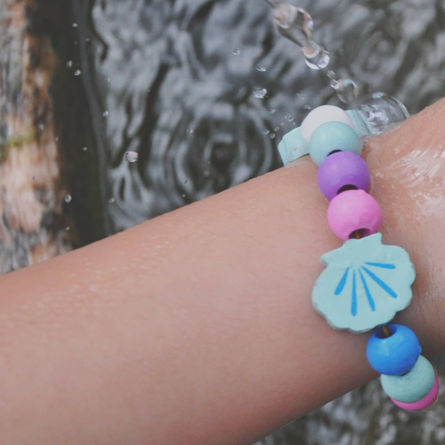 Colourful beaded bracelet with a shell charm on a wrist by a water source