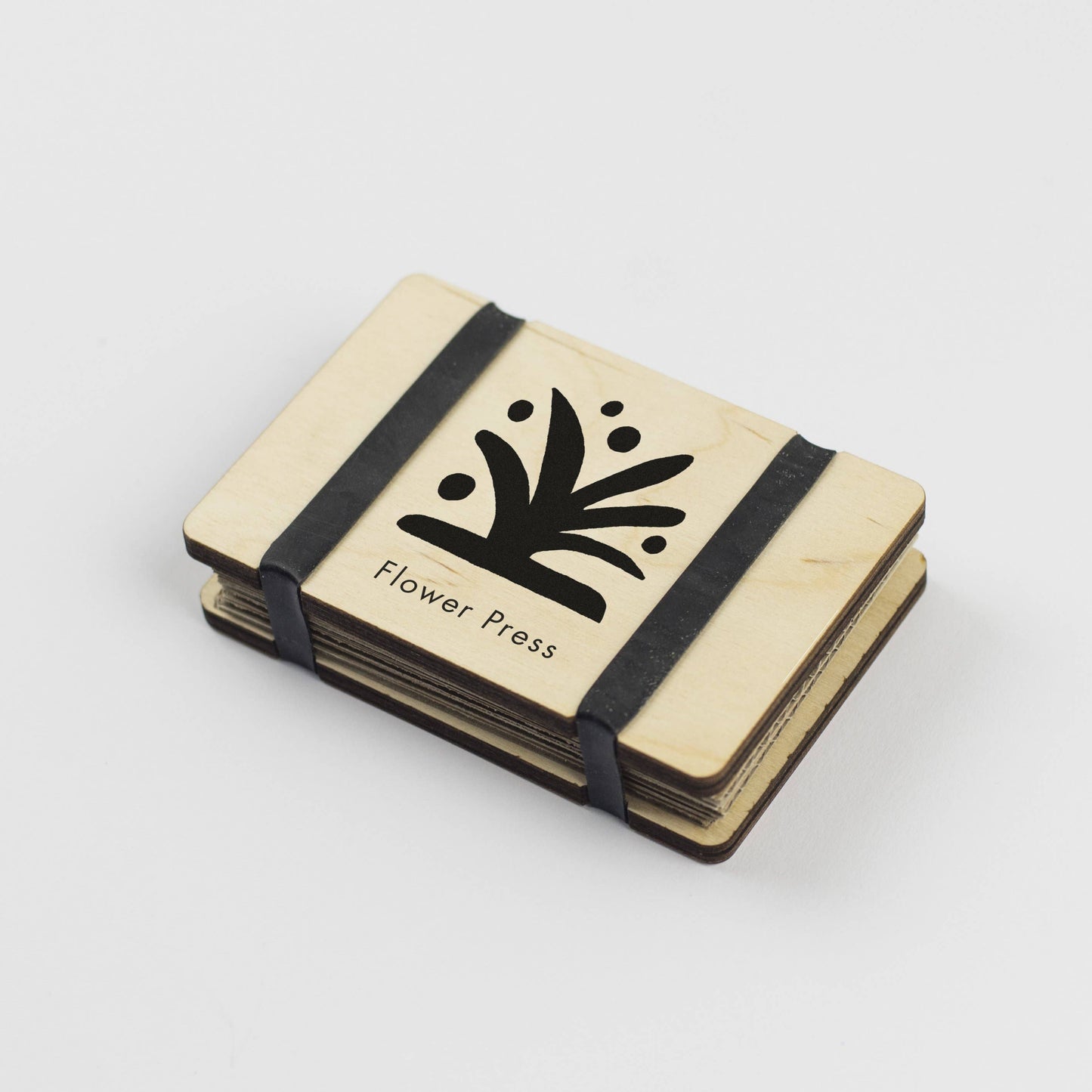 Pocket Size Flower press by Studio Wald. Black and white images of flowers on maple veneered sustainably sourced wood. Made in the UK. Fasten using the elastic bands and pop the press in your pocket. - The press comes complete with 5 sheets of corrugated card and 8 of sugar paper to give ample space to press flowers.