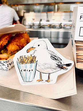 Die-cut greeting card featuring a cheeky seagull eyeing chips, paired with kraft envelope and gold sun ray embellishment.