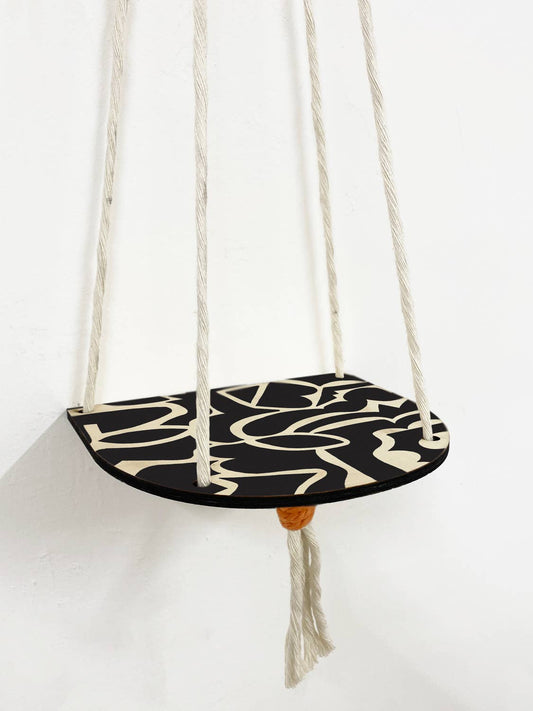 Close-up of abstract black pattern and orange macrame knots on hanging plant shelf