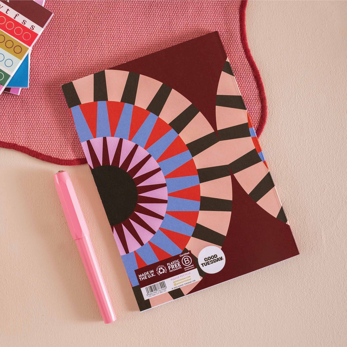 Colourful notebook with geometric design and 'Good Ideas' text, held by a person with a cup of coffee on a pink surface. UK Made. Eco friendly.