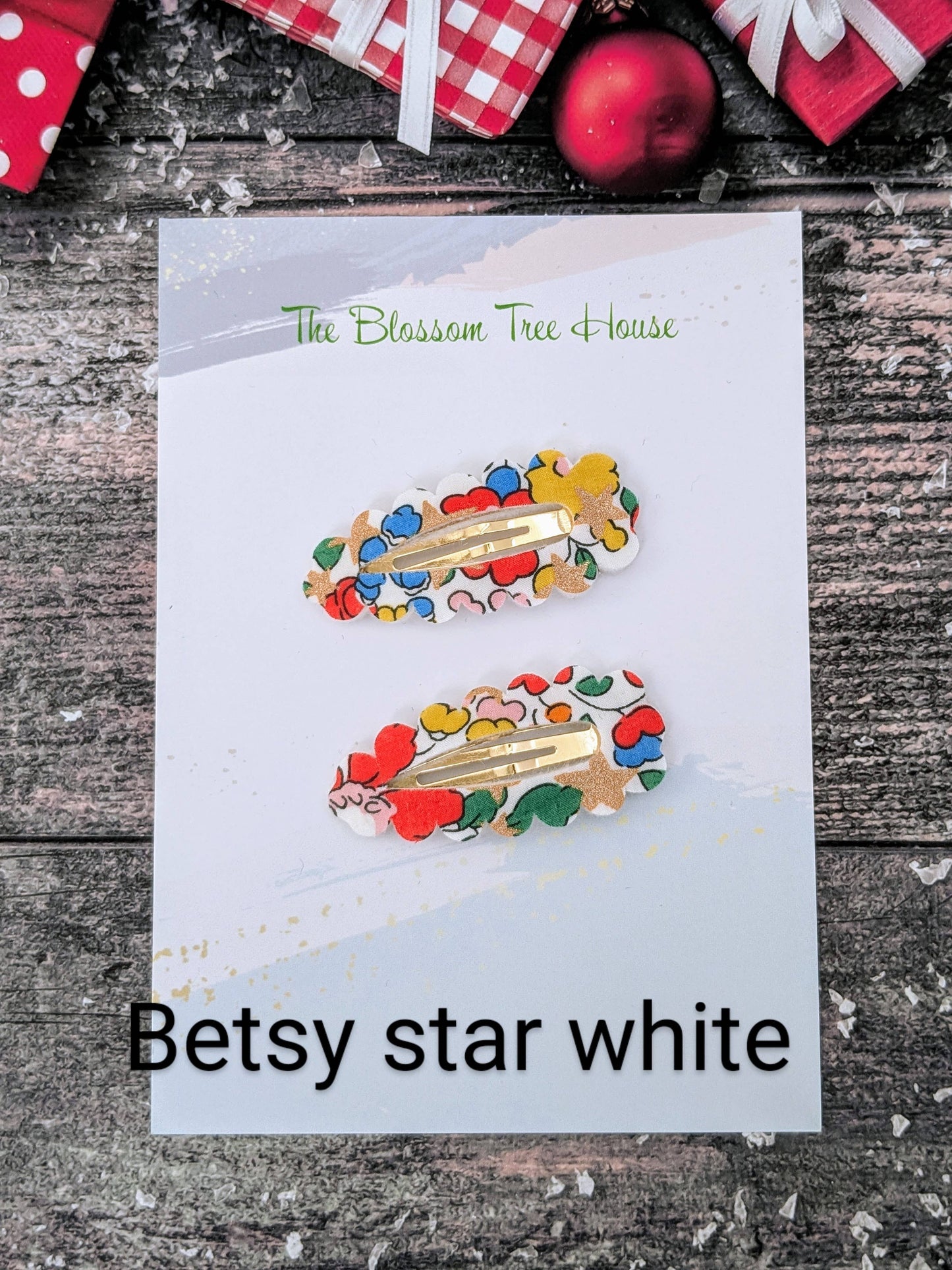 Colorful hair clips on a card with 'Betsy star white' text, placed on a wooden surface.