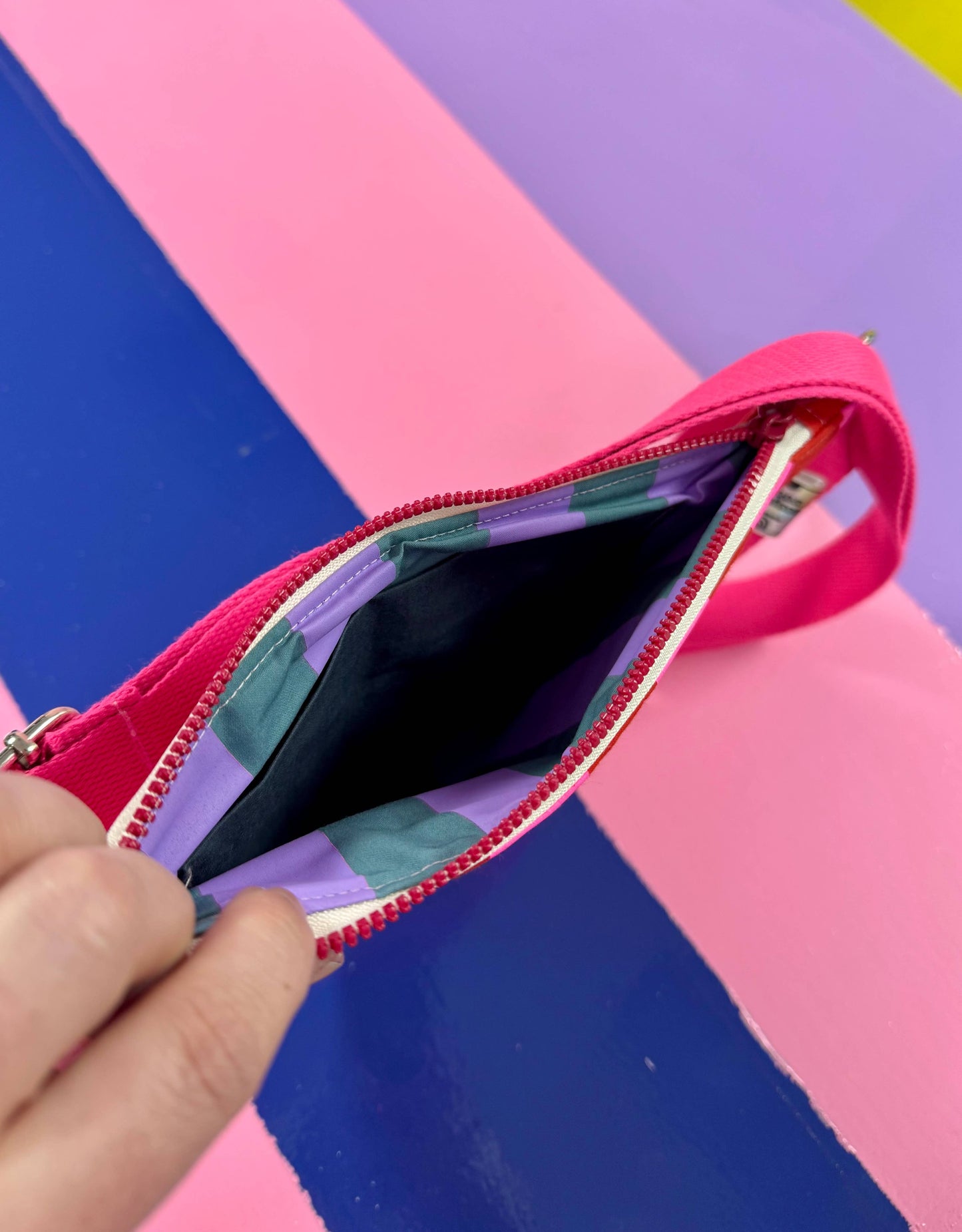 Pink and red striped waxed canvas sling bag, handprinted with artisan detail, featuring adjustable buckle straps and water-resistant finish.