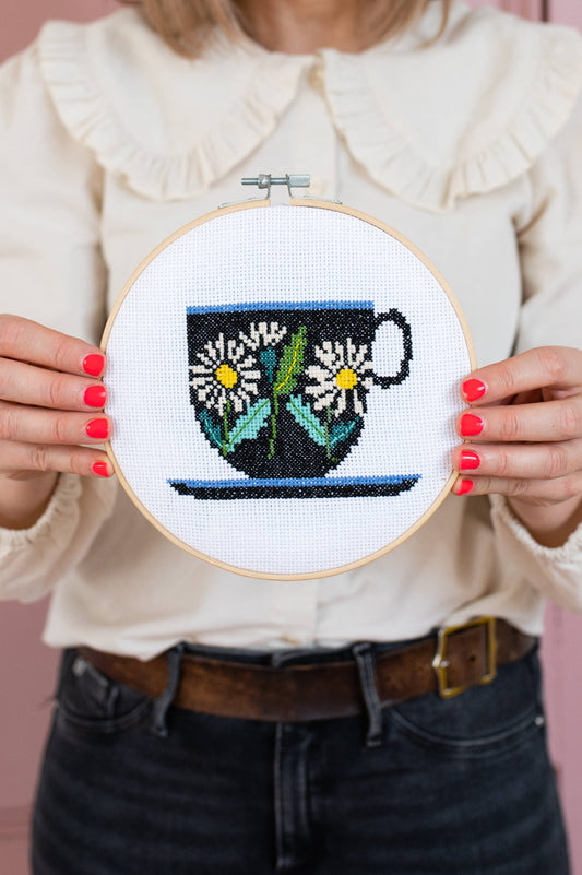 Contents of Brie Harrison Teacup Cross Stitch Kit laid out: hoop, fabric, thread, needle, instructions