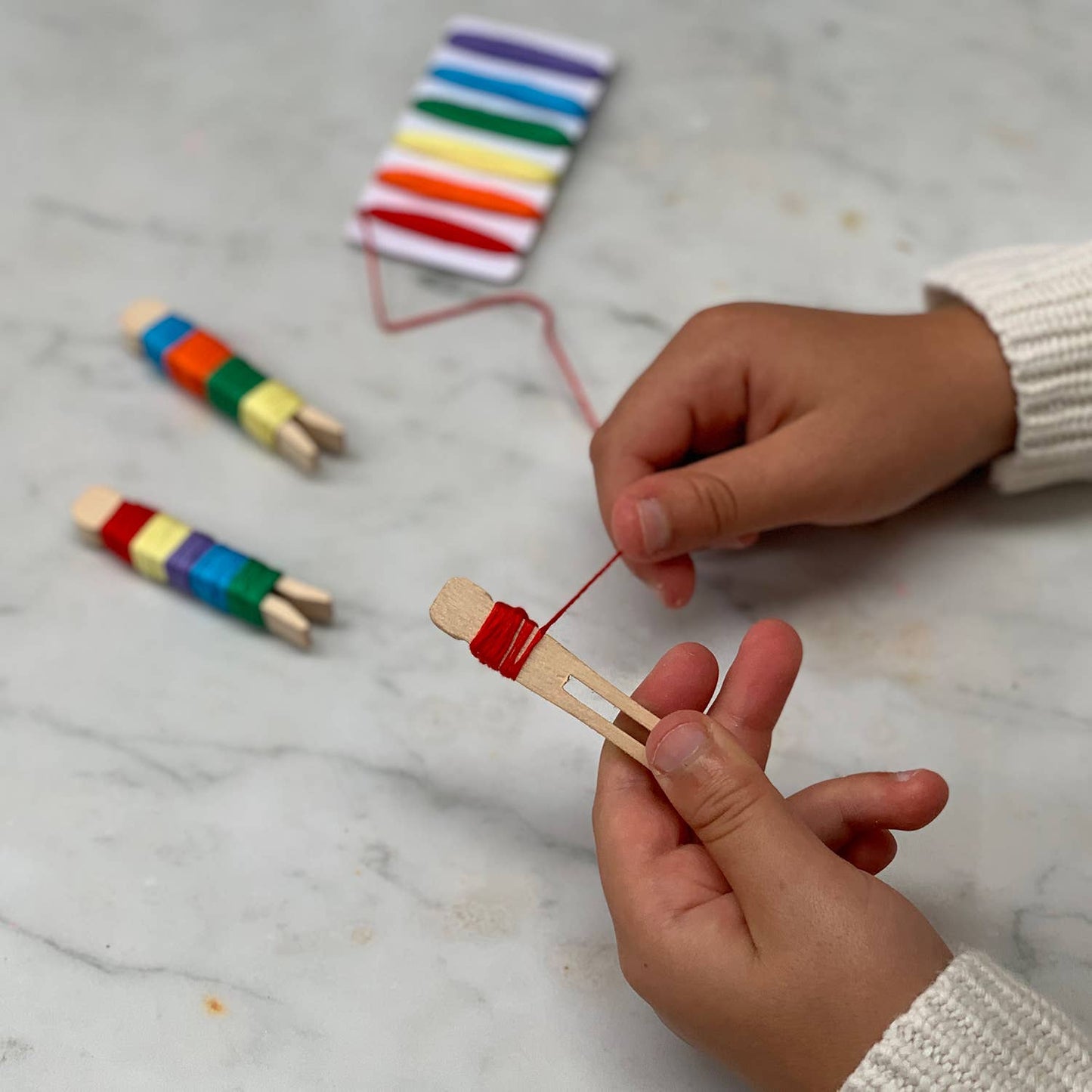 Child's hands threading colorful sticks with red thread on a marble surface