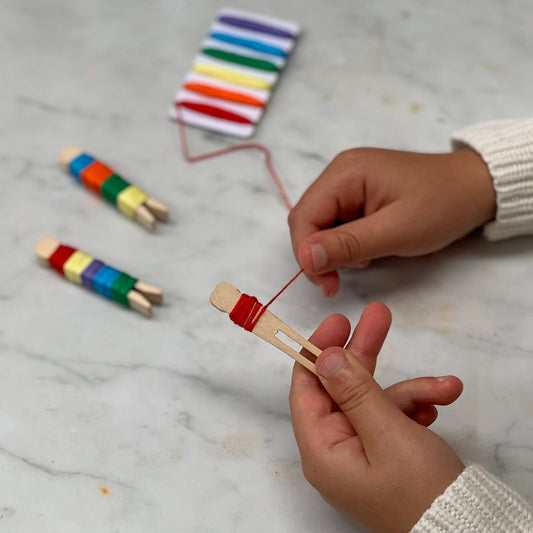 Child's hands actively threading a colourful wooden peg doll with red cotton thread