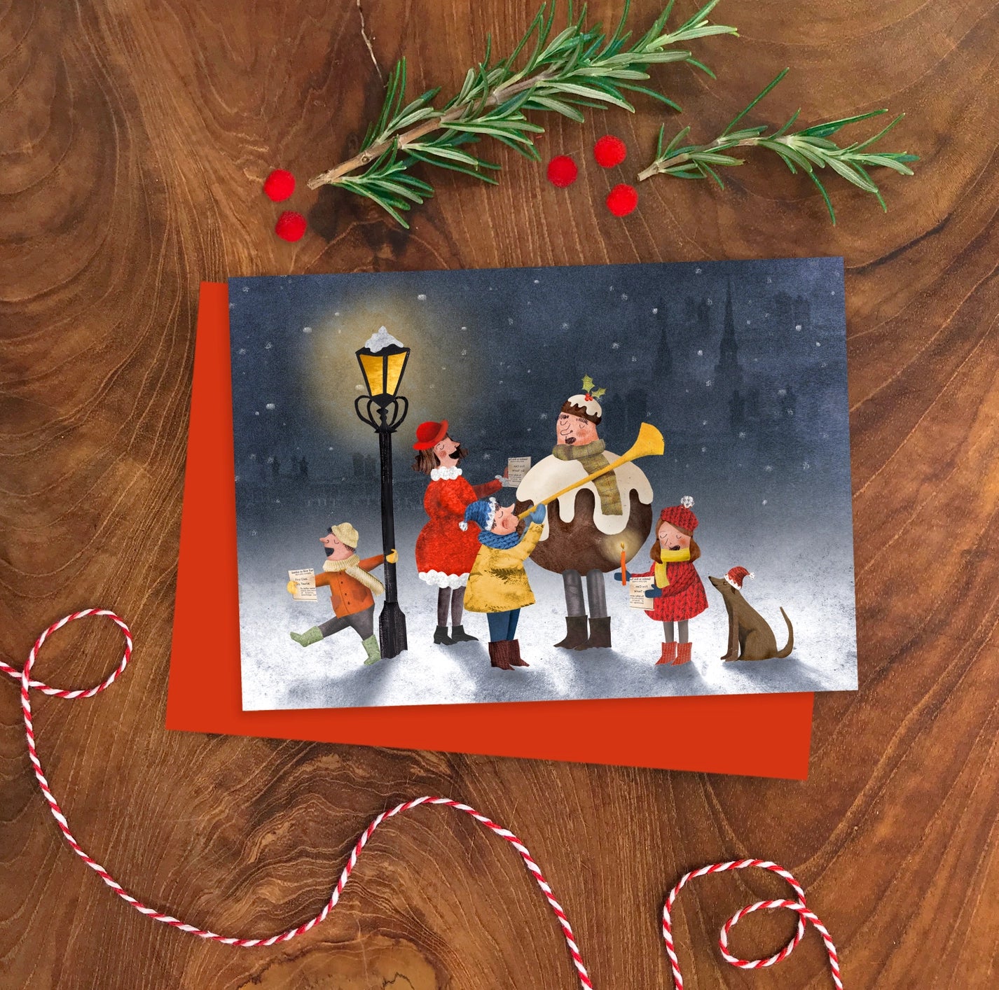 A6 illustrated Christmas card by Emily Nash showing a cheerful group of carol singers, printed on eco-certified matte card with a recycled kraft envelope.