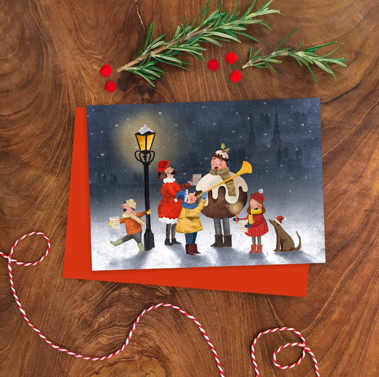 Close-up of Emily Nash's A6 illustrated Christmas card showing the cheerful carol singers design, paired with a recycled kraft envelope.