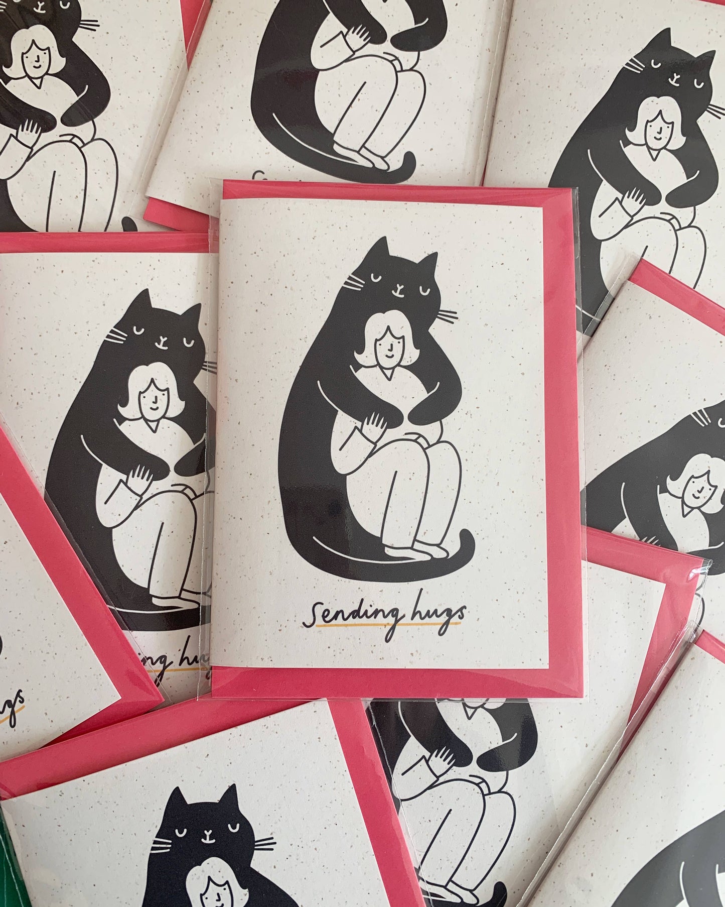 Black and white illustration of a huge black smiling cat cuddling a smaller smiling woman. with the words sending hugs at the bottom of the card.