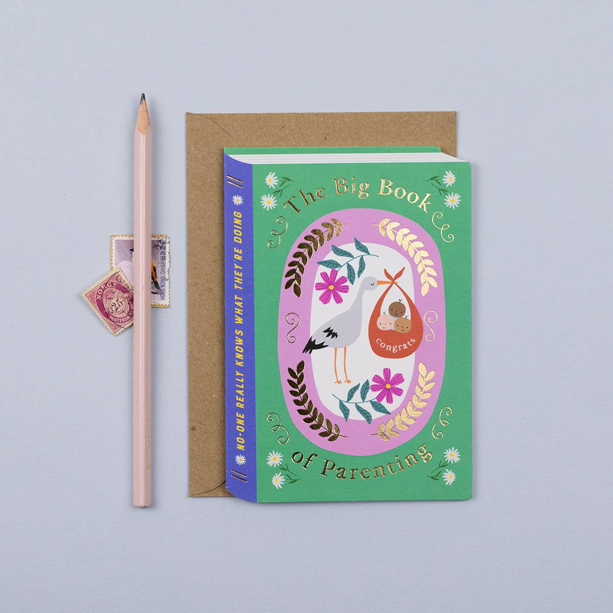 Fairytale New Parents Card with stork carrying three babies, 'The Big Book of Parenting' gold foil text, book-shaped, luxury kraft envelope.