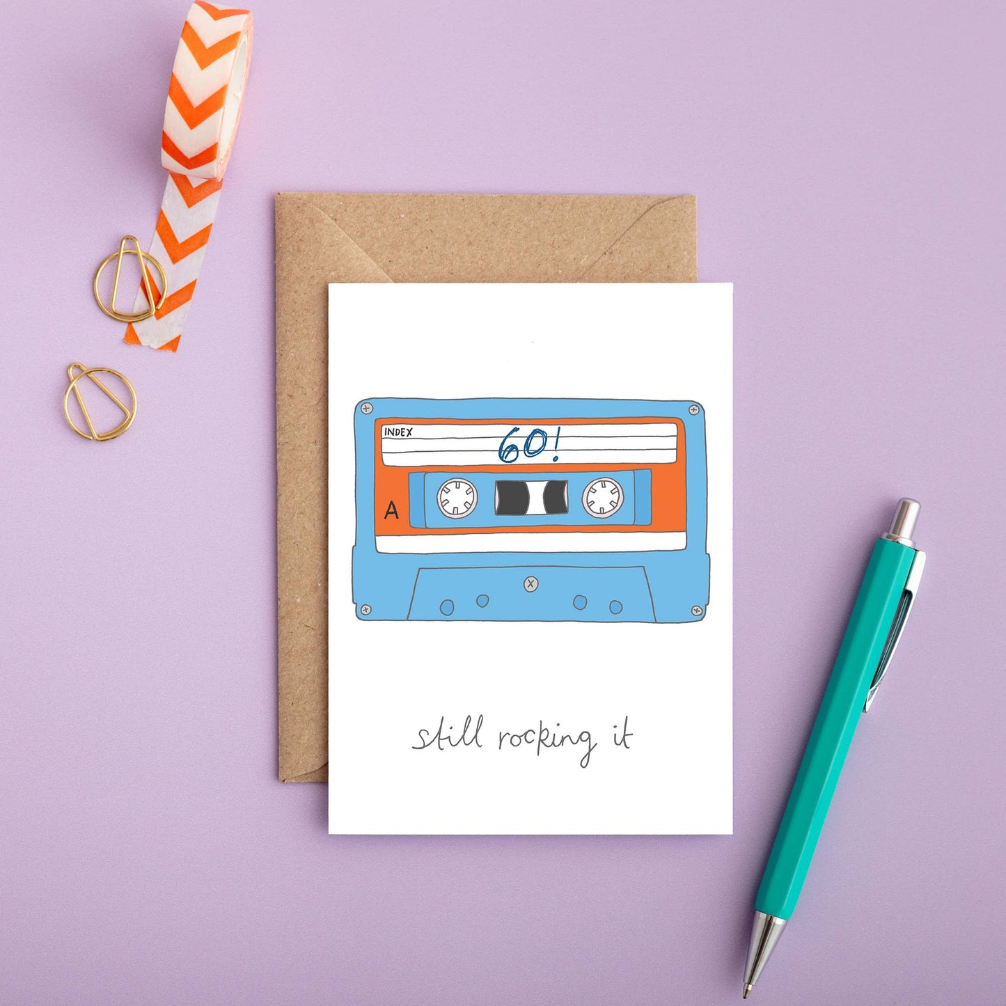 Funny 60th birthday card with hand-drawn illustration and caption 'Still Rocking It', printed on white sustainable card stock with kraft envelope.
